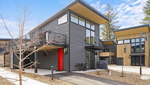 A modern two-story building with a red door, large windows, and a balcony. - Glacier State of Mind (Whitefish)