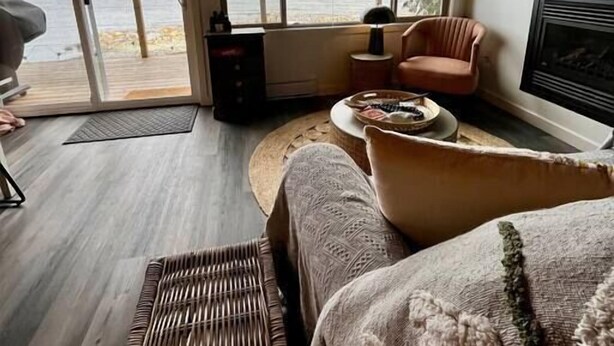 A cozy living room with a large window offering a view of the sea, a comfortable sofa, a television, and a fireplace. - DRIFT Studio / Oceanside / Firepit / Van Isle / BC (Comox)