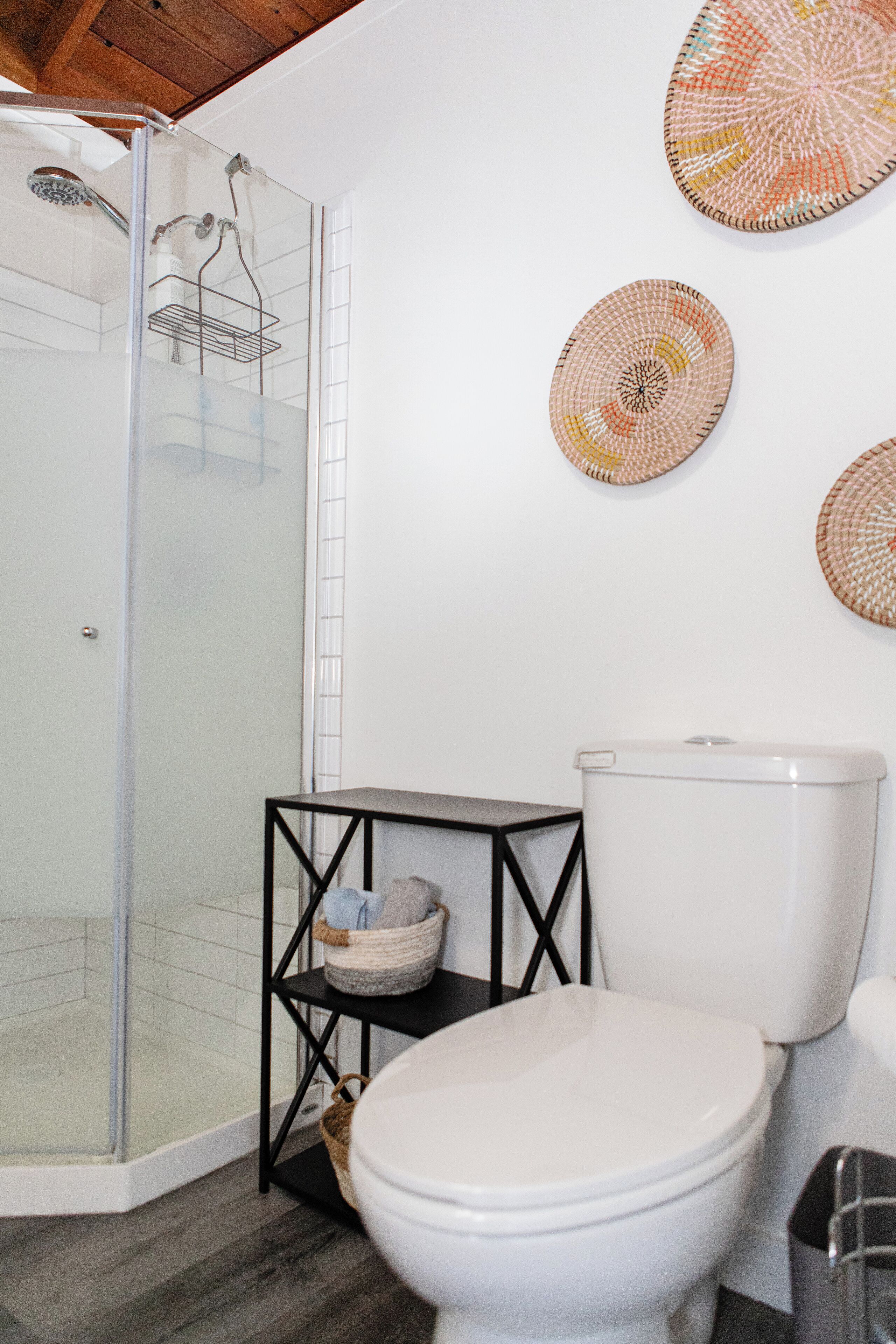 A bathroom with a glass shower enclosure, a white toilet, and a black metal shelf with baskets.