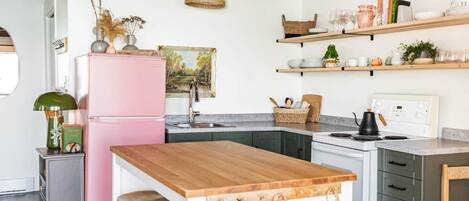 A kitchen with a wooden ceiling, a pink refrigerator, and a wooden island with hanging baskets.