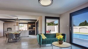 A modern living room with a sofa, dining table, and a view of a swimming pool.