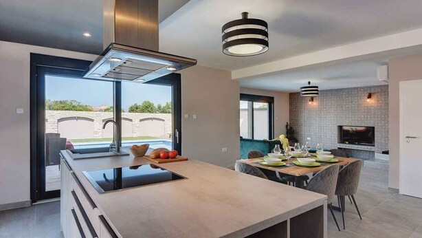 A modern kitchen with a central island, a dining area with a table set for four, and a TV mounted on the wall.