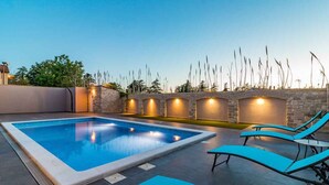 An outdoor swimming pool with lounge chairs and a stone wall with lights.