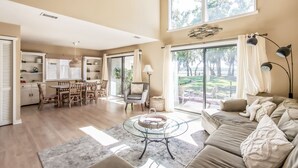 A spacious living room with a glass coffee table, a beige sofa, and a dining area with wooden furniture. - Exceptional 2 Bed/2.5 Bath Marshside Villa in Gated Resort! 5-Min Bike Ride to Private Beach Access! (Fernandina Beach)