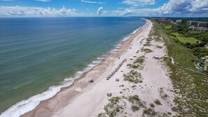 A beach with a row of beach umbrellas and lounge chairs, a fence, and buildings in the background. - Exceptional 2 Bed/2.5 Bath Marshside Villa in Gated Resort! 5-Min Bike Ride to Private Beach Access! (Fernandina Beach)