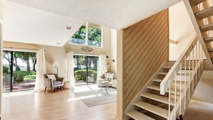 A spacious living room with a wooden staircase, large windows, and a view of the outdoors. - Exceptional 2 Bed/2.5 Bath Marshside Villa in Gated Resort! 5-Min Bike Ride to Private Beach Access! (Fernandina Beach)