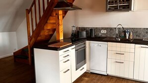 A kitchen with a wooden staircase, a built-in oven, a dishwasher, and a sink with a tiled backsplash.