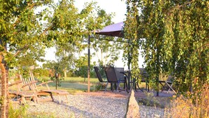 An outdoor seating area with a table and chairs under a pergola, surrounded by gravel and greenery.