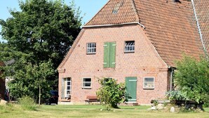 A brick building with a sloped roof, green shutters, and a small porch area.
