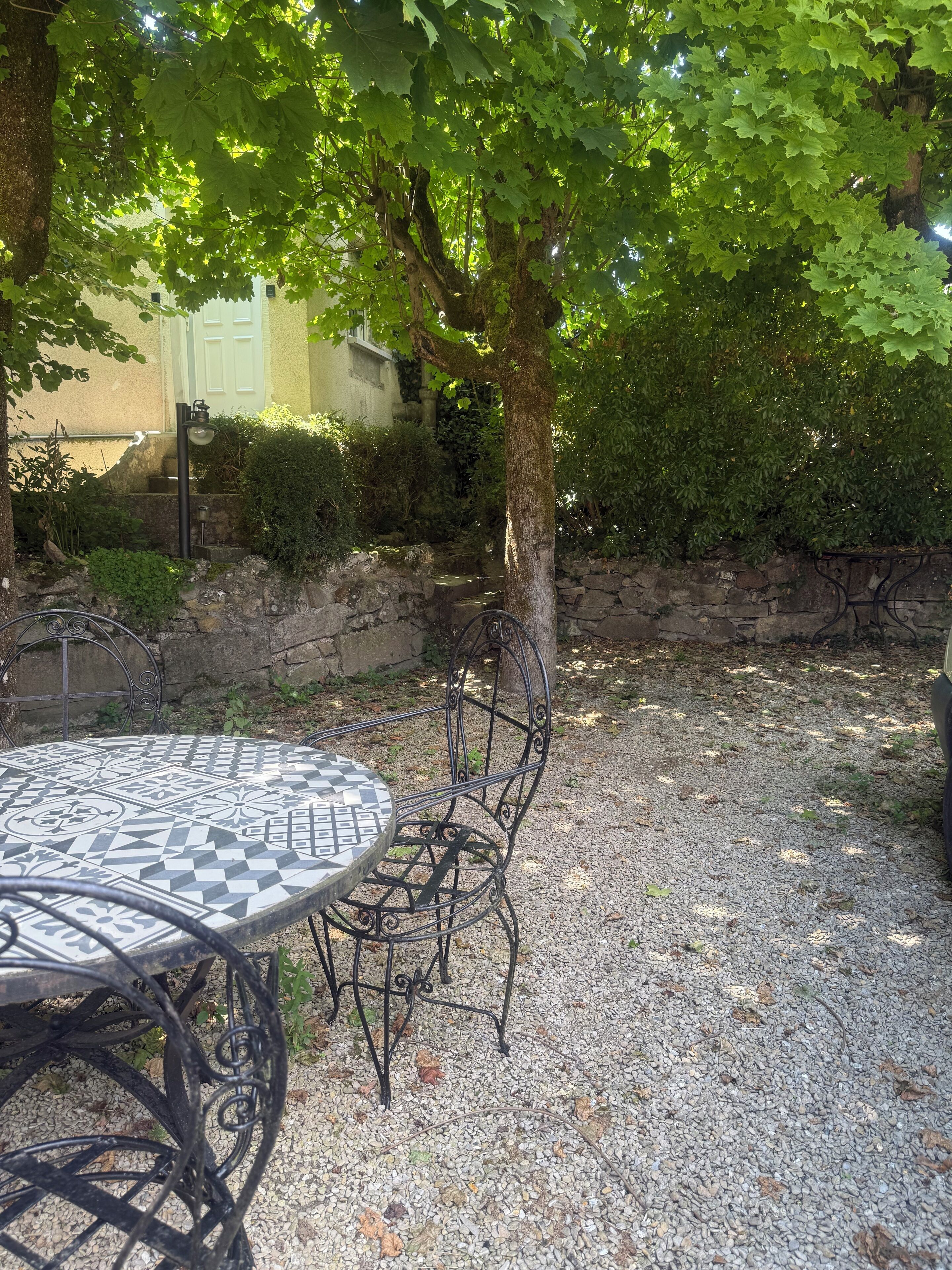 Une terrasse avec une table ronde et des chaises, entourée de gravier et d’un muret en pierre.