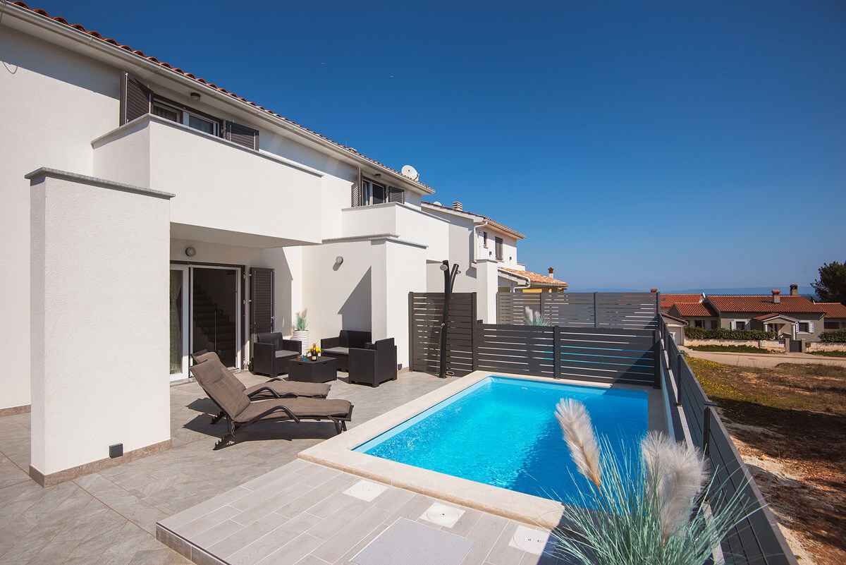 Ein modernes Haus mit Schwimmbad, Sitzgelegenheiten im Freien und Meerblick.