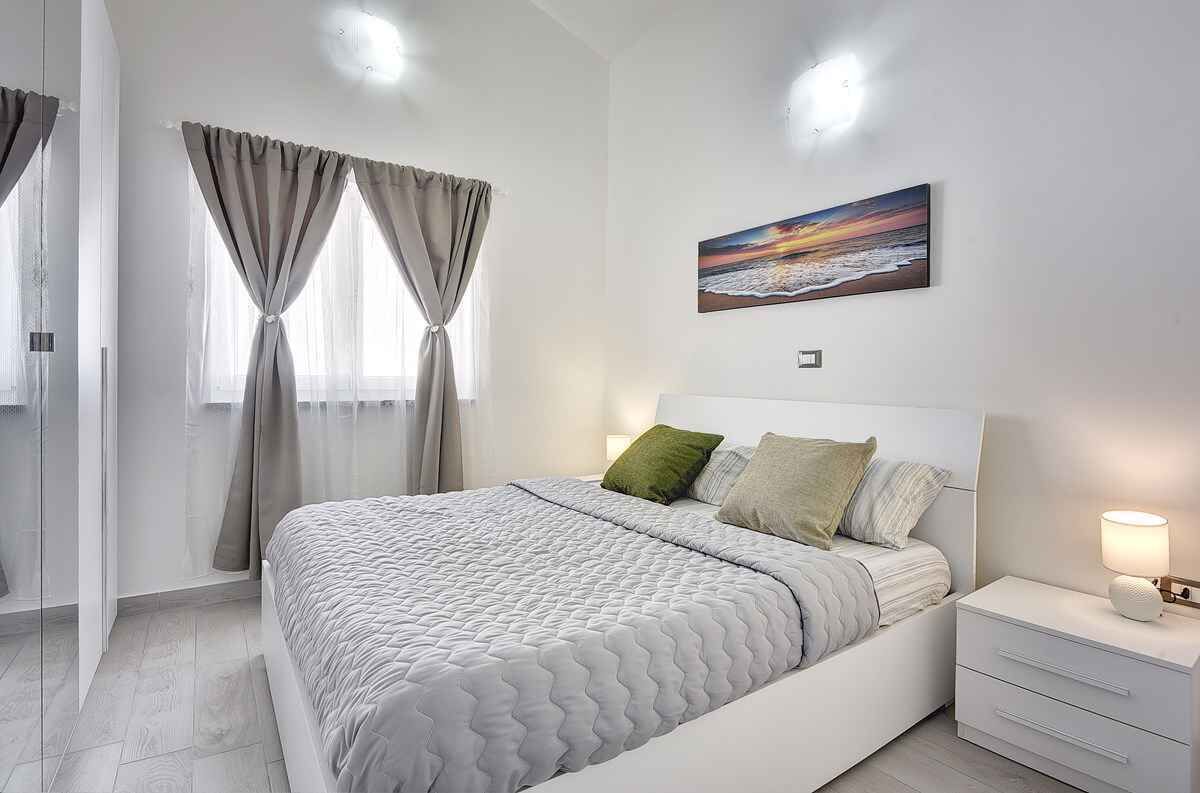 Ein modernes Schlafzimmer mit einem großen Bett, einem Nachttisch mit Lampe und einem Gemälde an der Wand.