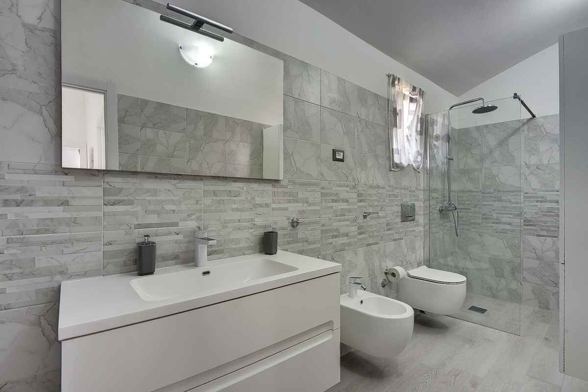 Une salle de bain moderne dotée d’un meuble-lavabo à deux vasques, d’un bidet, de toilettes et d’une douche à l’italienne.