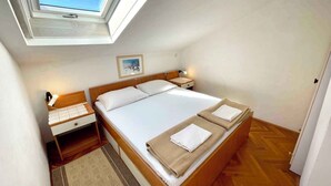 Un dormitorio con tragaluz, una cama con dos almohadas, una mesita de noche con lámpara y una pequeña alfombra.