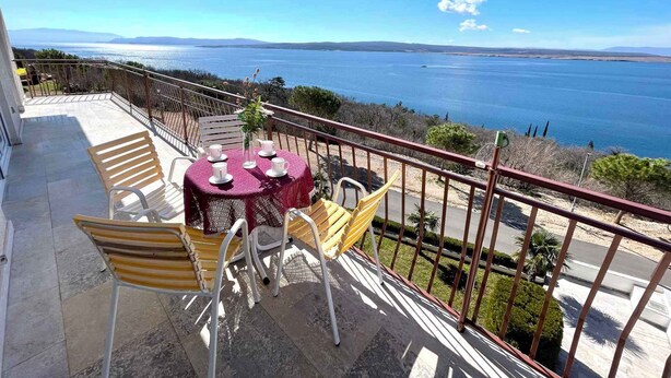 Een balkon met een tafel voor vier personen, uitkijkend op een wateroppervlak en het landschap in de verte.