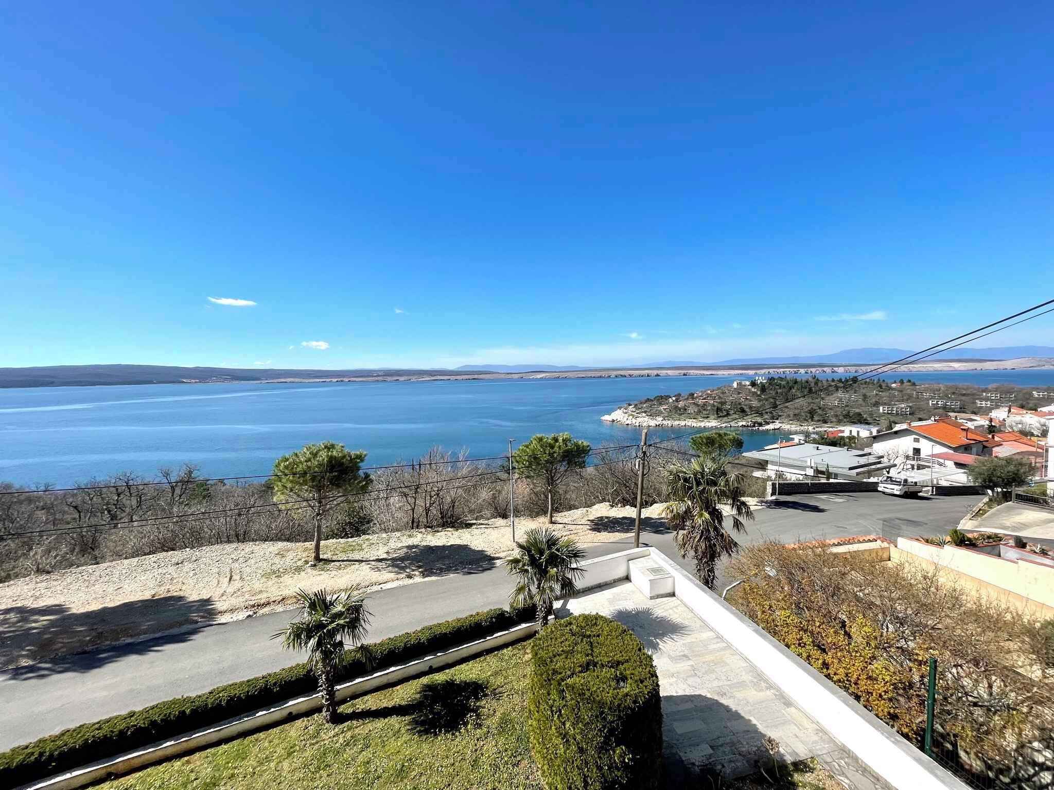 A coastal view with a clear sky, a road leading to a parking area, and a body of water in the distance.