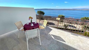 Ein Balkon mit Tisch und Stühlen, der auf ein Gewässer und hügelige Landschaften blickt.