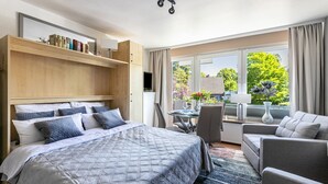 Habitación de hotel moderna con cama, escritorio, sofá y un amplio ventanal con vistas a zonas verdes.