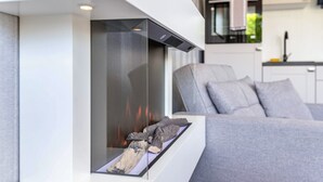 Una sala moderna con chimenea, un sofá y una cocina al fondo.