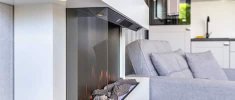 A modern living room with a fireplace, a sofa, and a kitchen in the background.