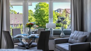 Una habitación moderna con una mesa de comedor, sillas, un sofá y ventanas grandes con cortinas.