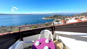 Un balcon avec une table et des chaises donnant sur une ville côtière et une vaste étendue d’eau.