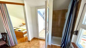 Une pièce avec un plancher en bois, un lit, une chaise et un espace douche.