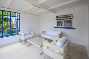 A room with two white sofas, a glass coffee table, and a window with blue frames.