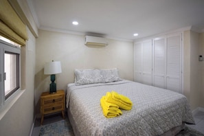 A bedroom with a bed, a nightstand, a lamp, an air conditioning unit, and a window.
