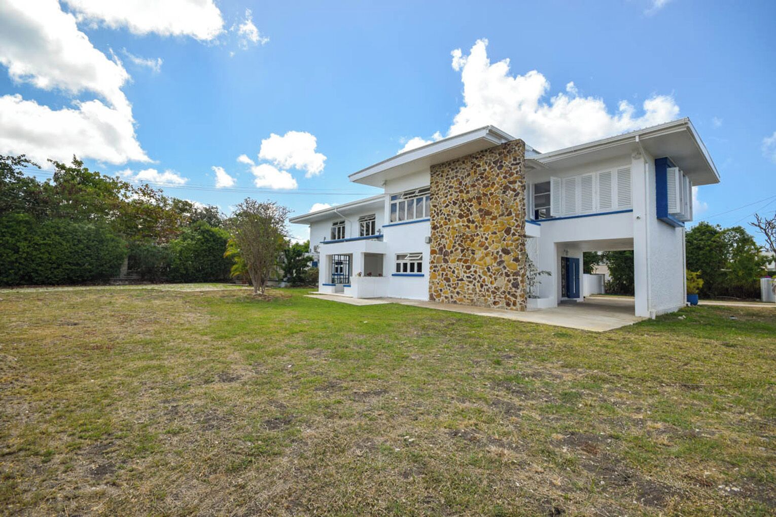 Uma casa moderna de dois andares com fachada de pedra, telhado plano e gramado bem cuidado.