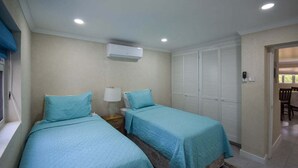 Une chambre avec deux lits, une table de chevet avec une lampe, un appareil de climatisation et un placard avec des portes à persiennes.
