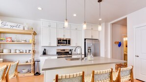Una cocina moderna con armarios blancos, un refrigerador de acero inoxidable, un microondas y una isla grande con taburetes de bar.