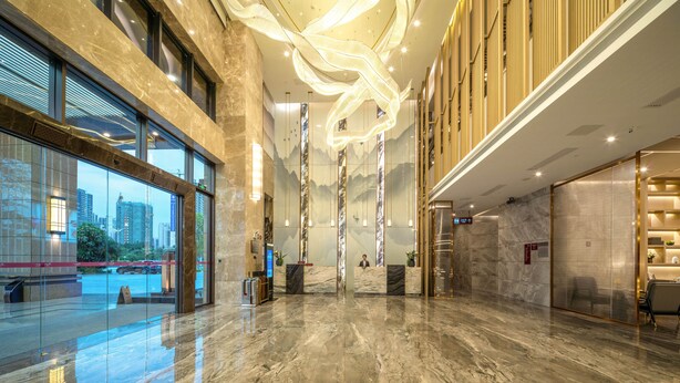 A spacious lobby with a marble floor, large windows offering a city view, and a modern ceiling design.