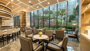 A modern interior with a bar area, seating, and large windows offering a view of greenery and buildings.