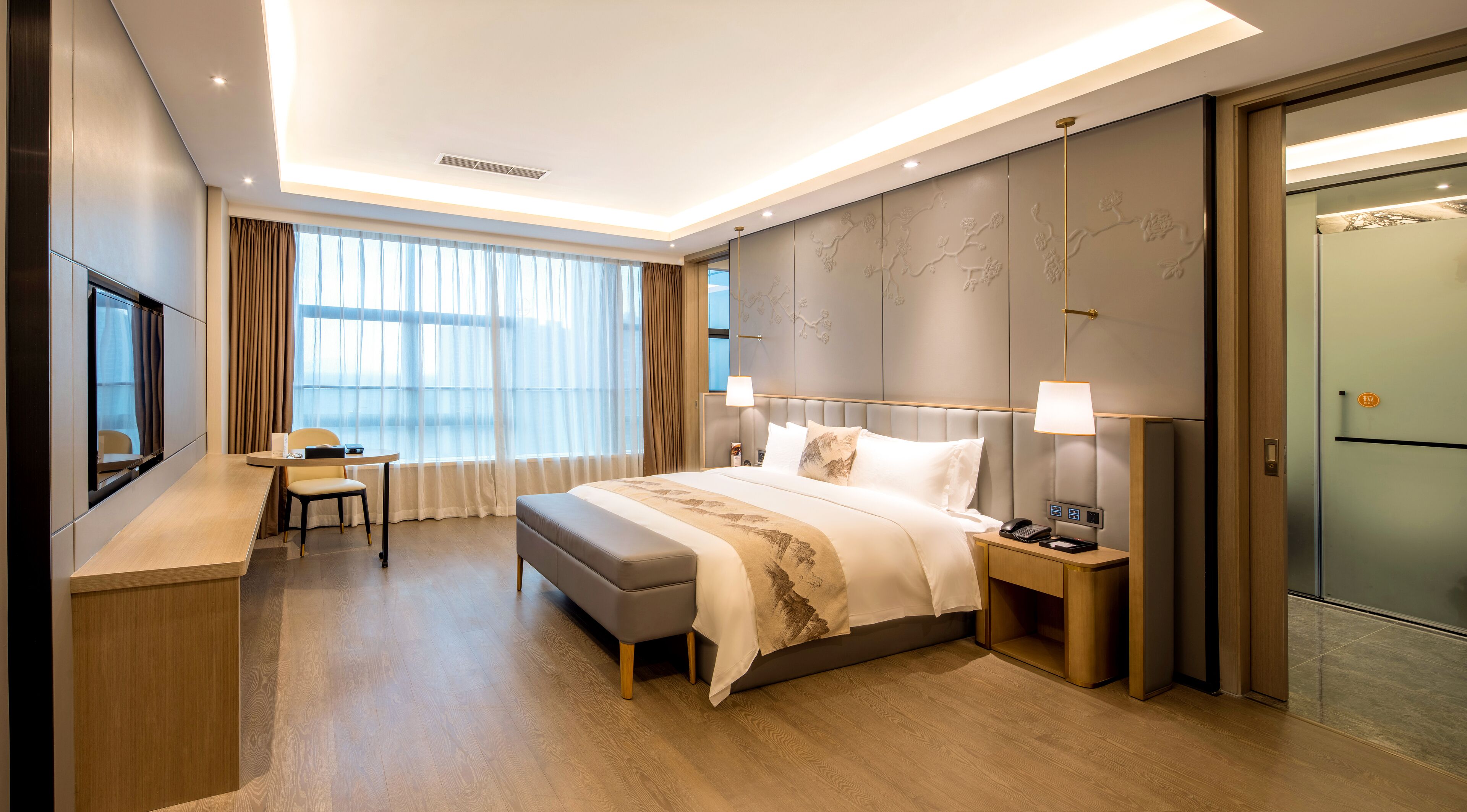 Ein modernes Hotelzimmer mit einem großen Bett, Nachttischen, einem Schreibtisch und einem großen Fenster mit Vorhängen.