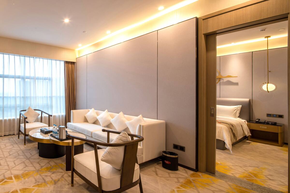 Ein modernes Hotelzimmer mit einer Couch, Sesseln, einem Couchtisch, einem Fernseher und einem Bett.
