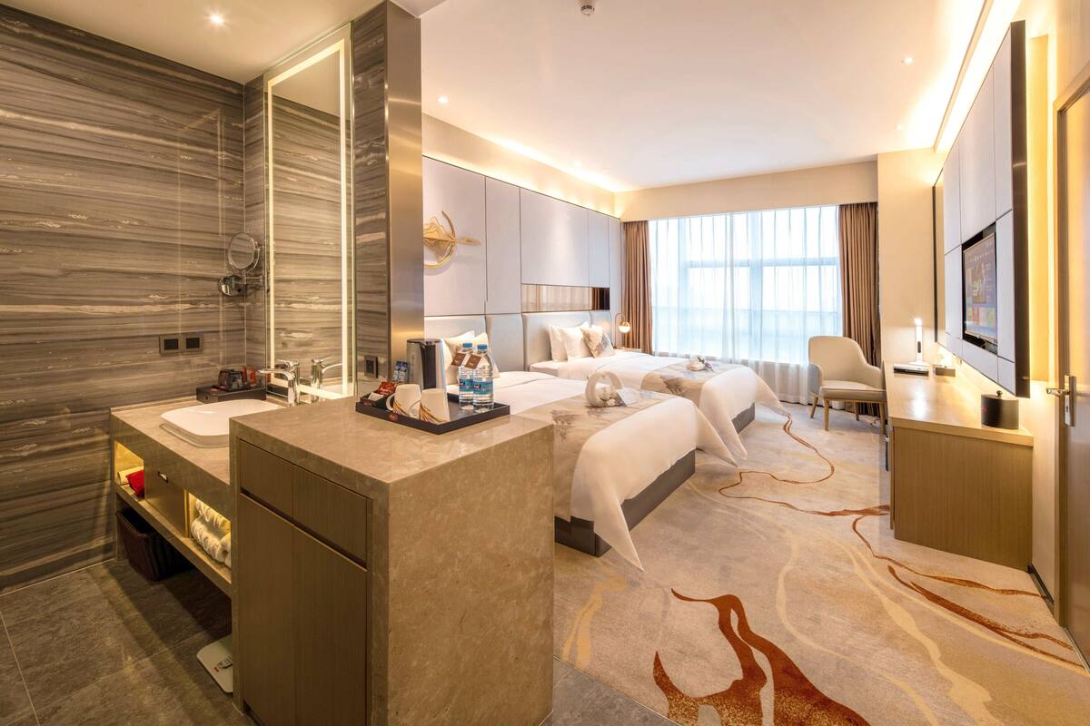 Ein modernes Hotelzimmer mit Marmorwand, einem großen Bett, einer separaten Couch, einem Fernseher und einem Badezimmer mit Marmor-Waschtisch.