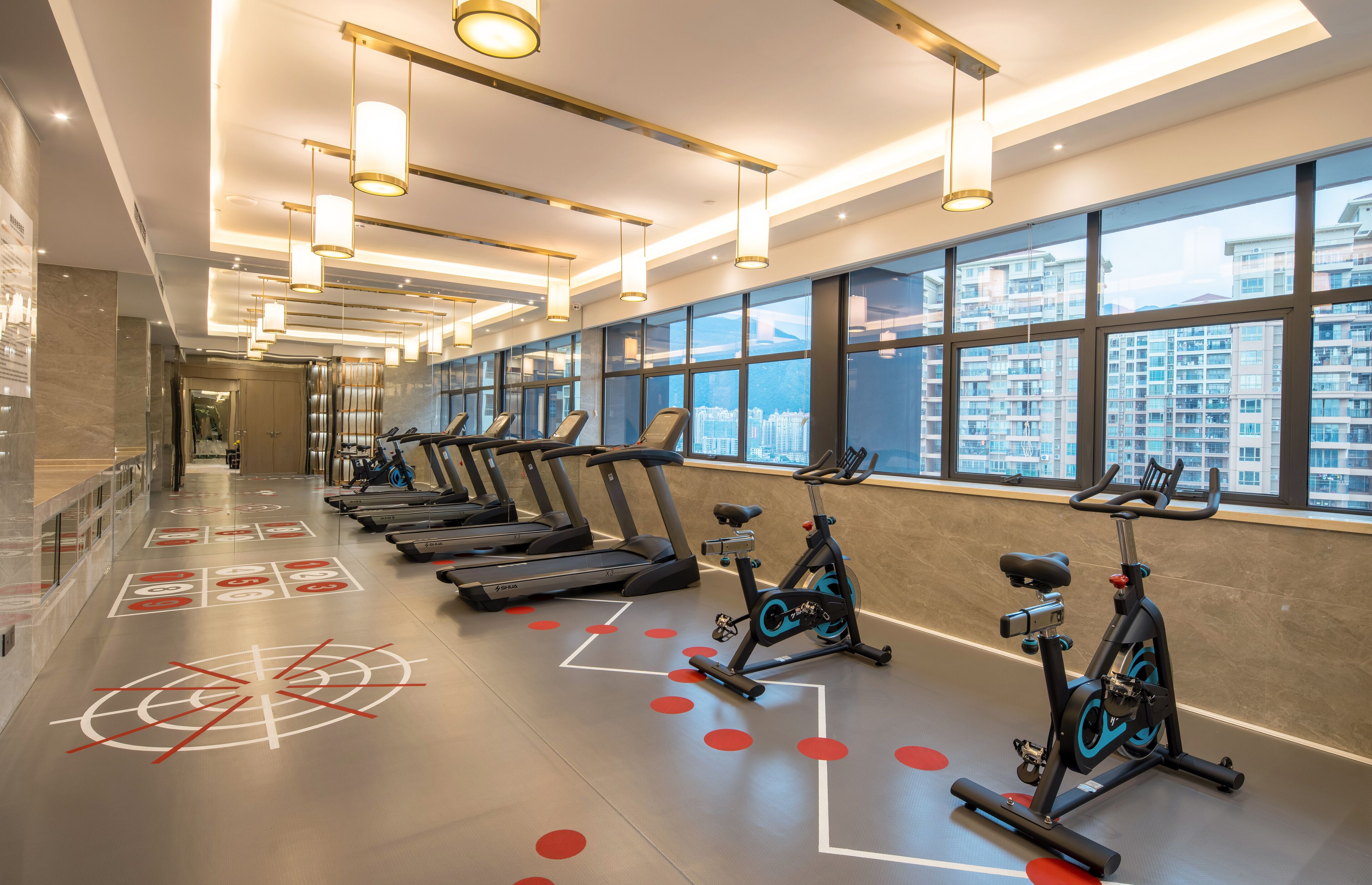 A modern gym with treadmills, stationary bikes, and a large window offering a city view.