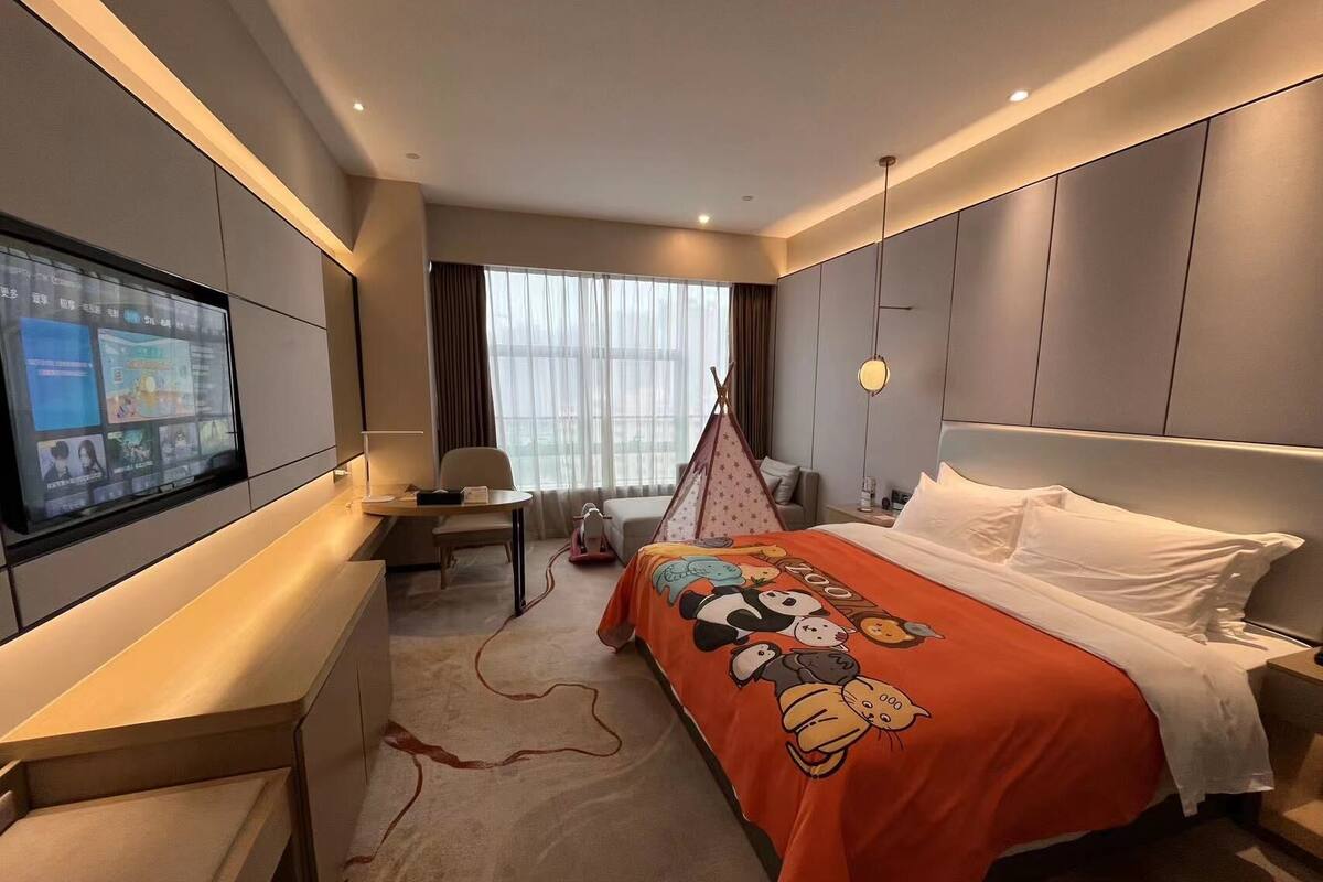 Ein Hotelzimmer mit Bett, Schreibtisch, Fernseher und einem Fenster mit Vorhängen.