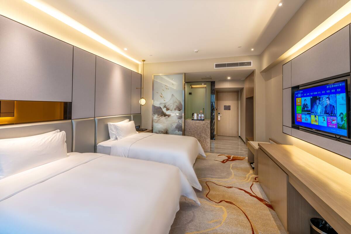 Ein Hotelzimmer mit zwei Betten, einem Wandfernseher und einem Flur, der zu einem Badezimmer führt.
