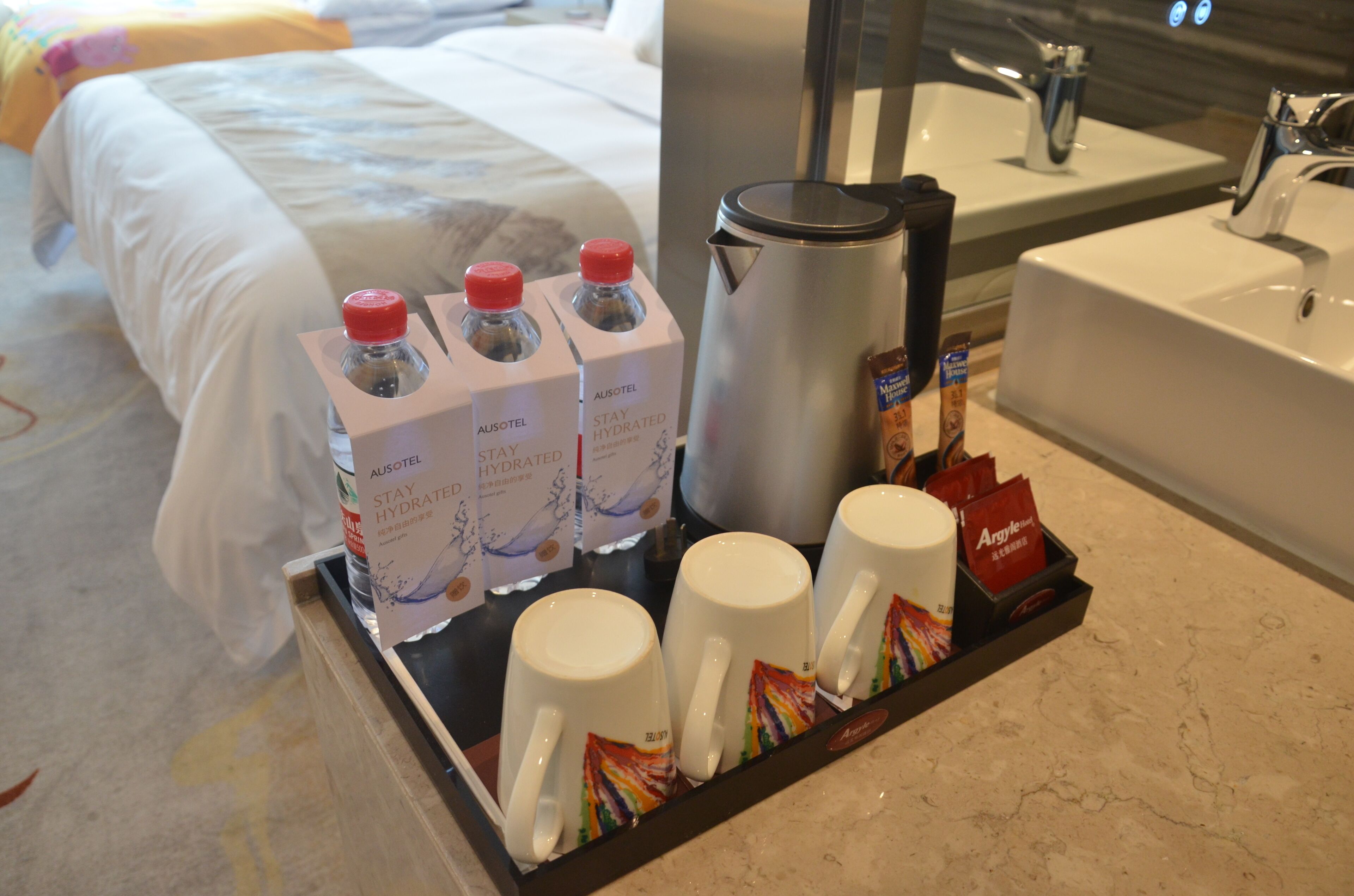 A hotel room with a bed, a tray table with water bottles, a coffee maker, and a tray with coffee cups and tea bags.