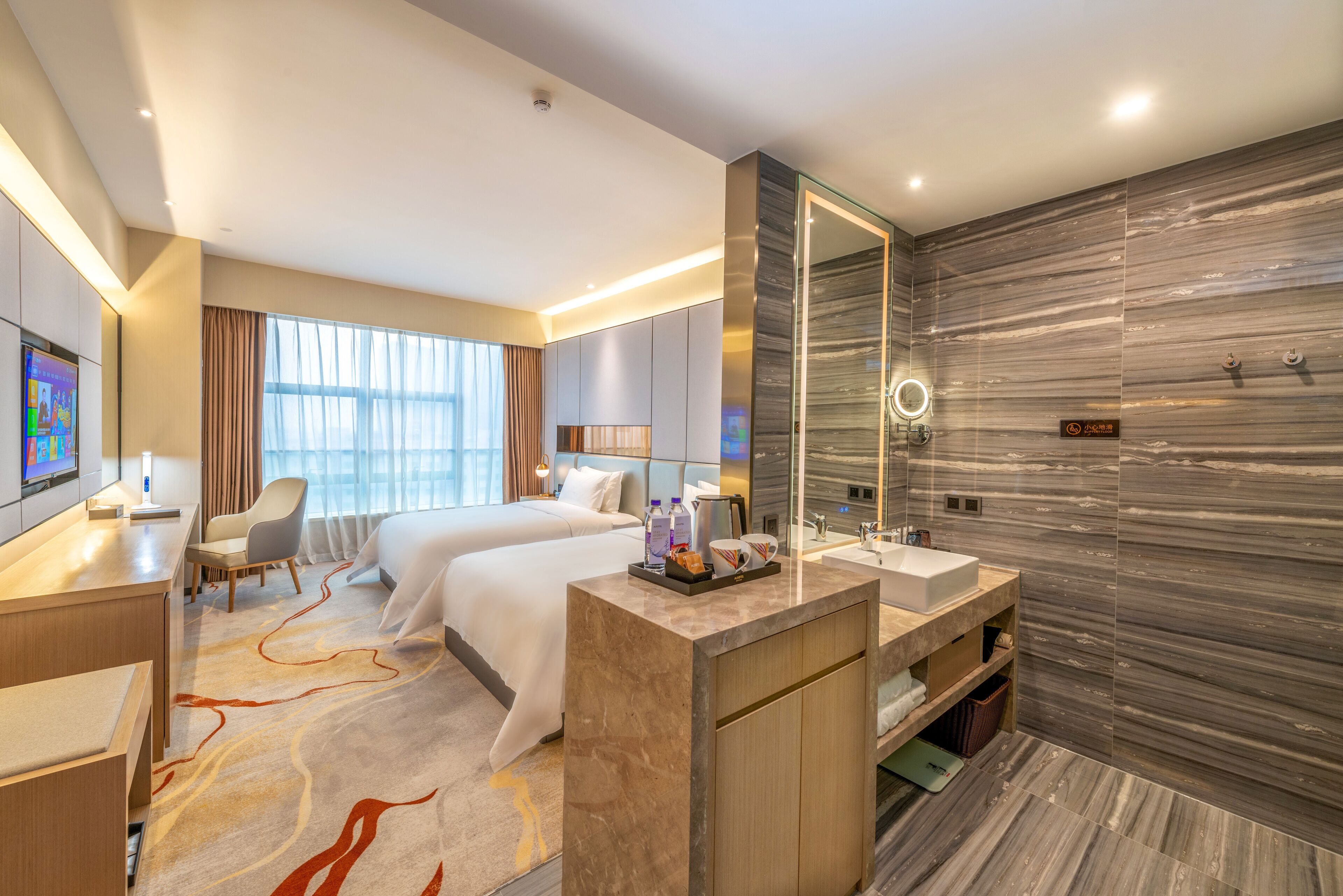 Una habitación de hotel moderna con dos camas, un escritorio, un baño con un espejo grande y vistas a la ciudad.