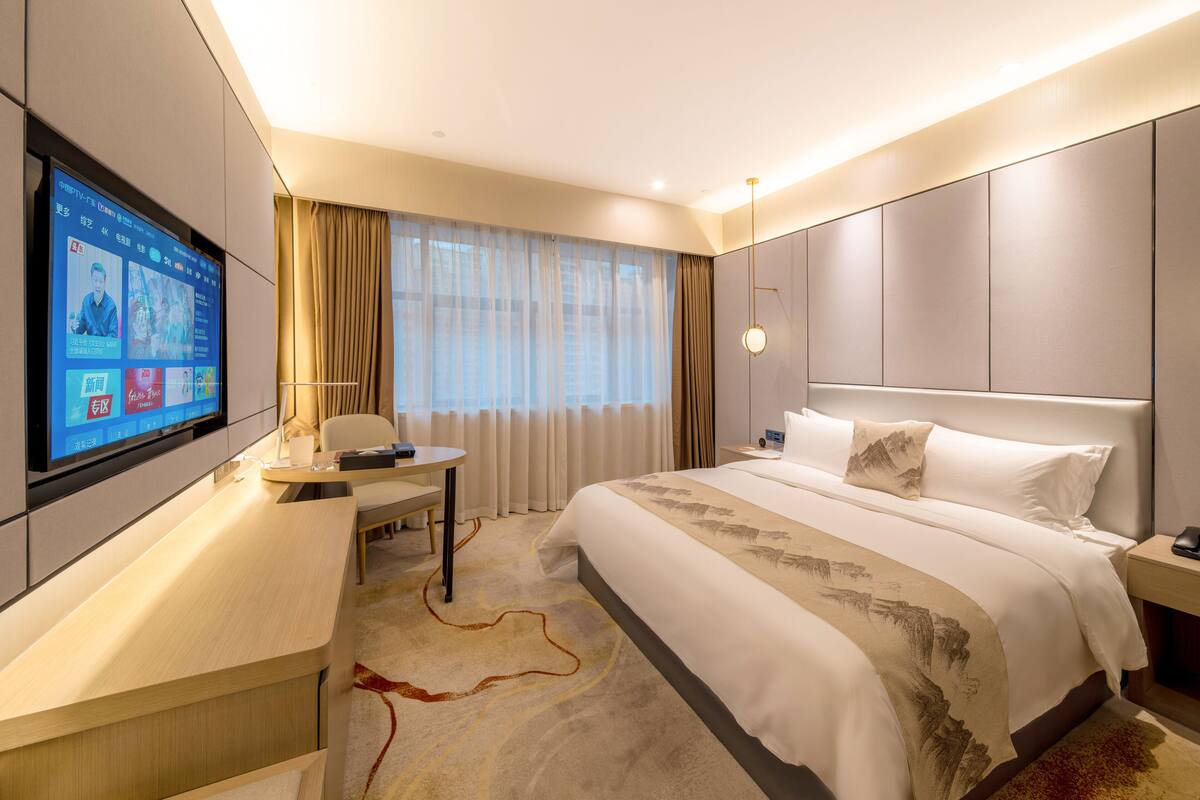 Ein modernes Hotelzimmer mit einem großen Bett, einem Schreibtisch und einem an der Wand befestigten Fernseher.