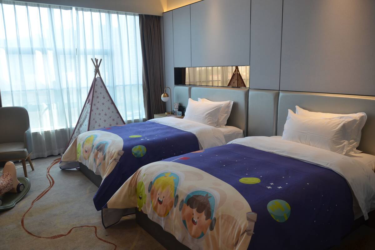 Ein Hotelzimmer mit zwei Betten, einem fensterbelaubten Fenster, einem Nachttisch, einer Lampe und einer Teepeebekleidung.