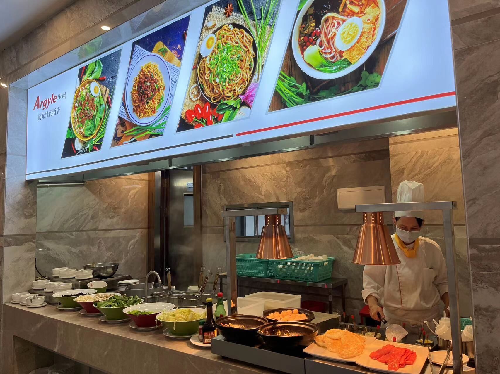 A buffet area with various dishes displayed on a counter, a chef preparing food, and a menu above with images of dishes.