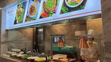 A buffet area with various dishes displayed on a counter, a chef preparing food, and a menu above with images of dishes.
