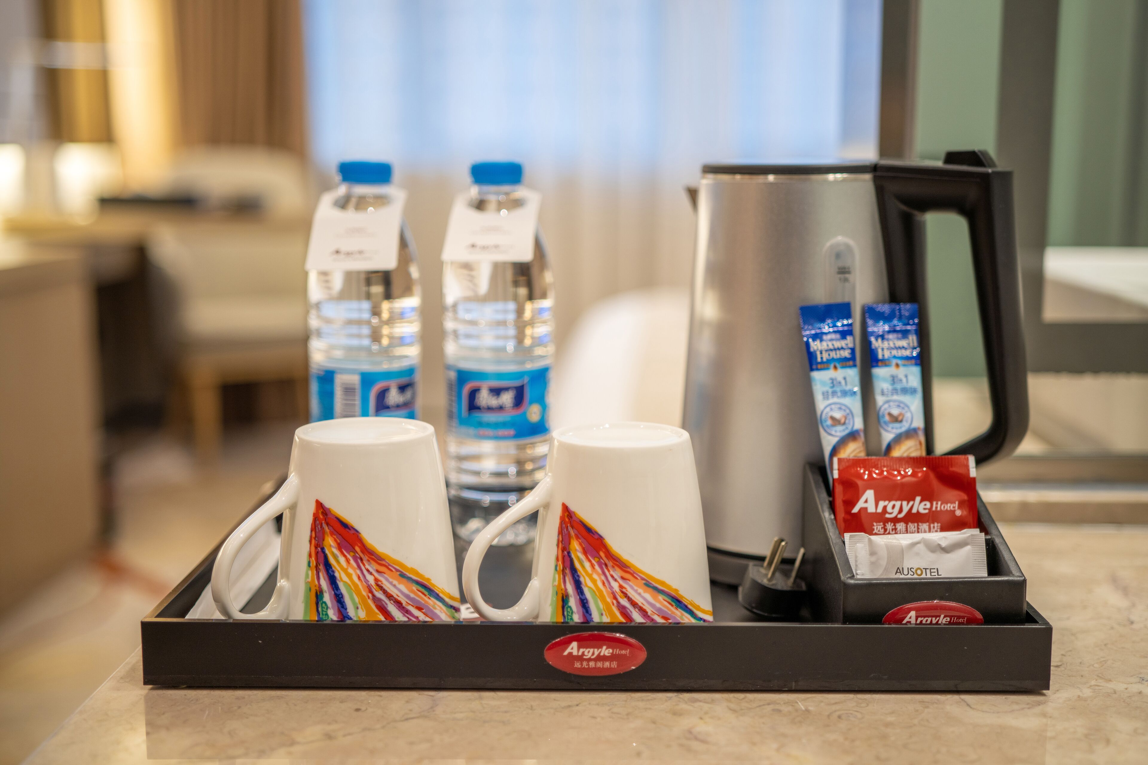 En bakke med kaffemaskine, to vandflasker og en kop med et farverigt mønster.