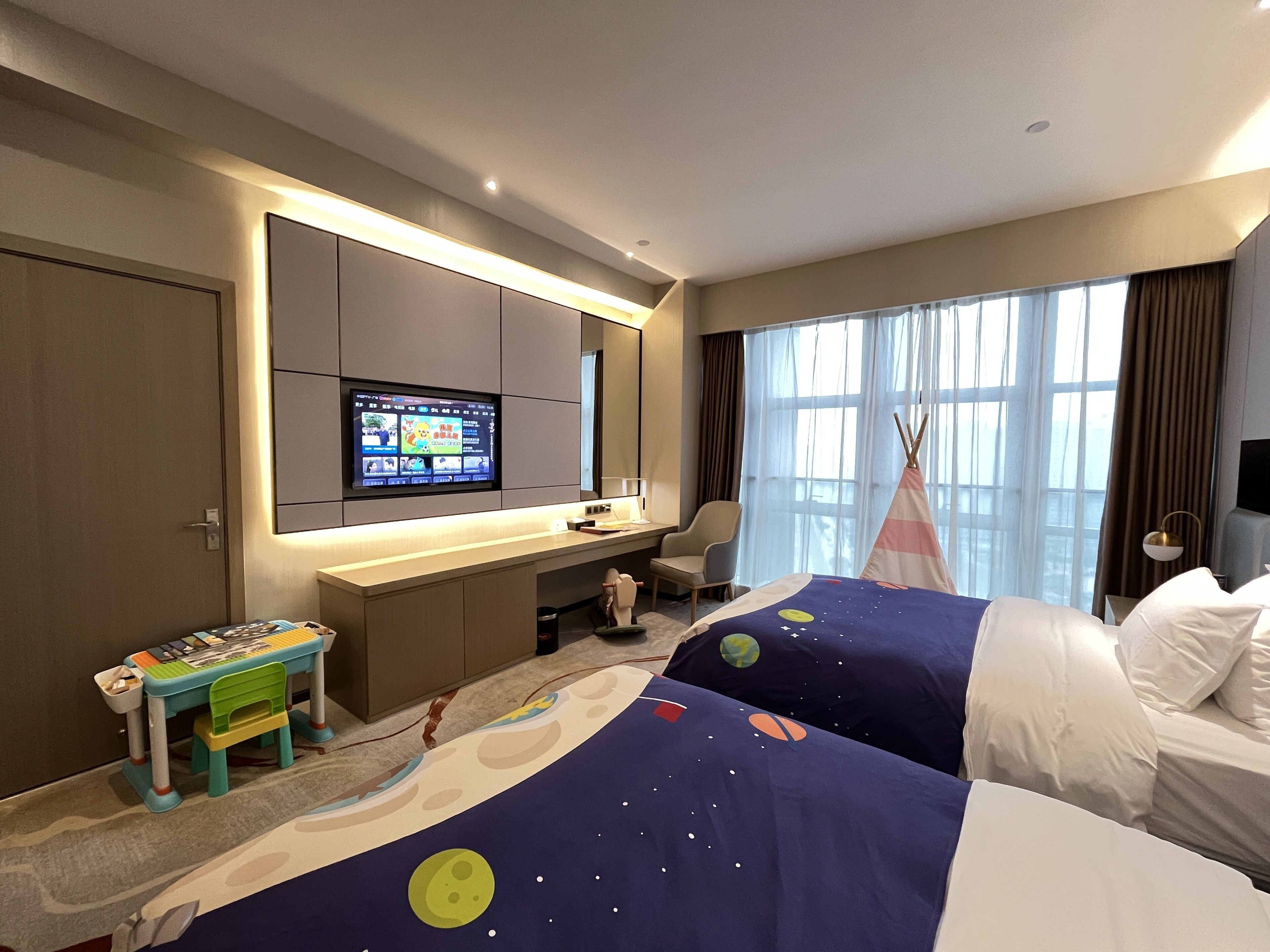 Una habitación de hotel con cama, escritorio con ordenador, televisor, mesita y ventana con cortinas.