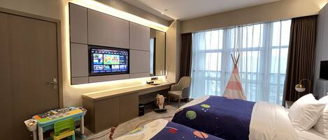 Una habitación de hotel con cama, escritorio con ordenador, televisor, mesita y ventana con cortinas.