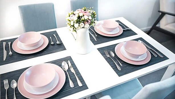 Ett matbord dukat med rosa tallrikar, silverbestick och en vas med blommor.